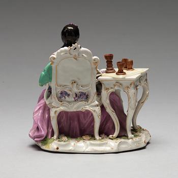 A Meissen porcelain figure of a lady by a table.