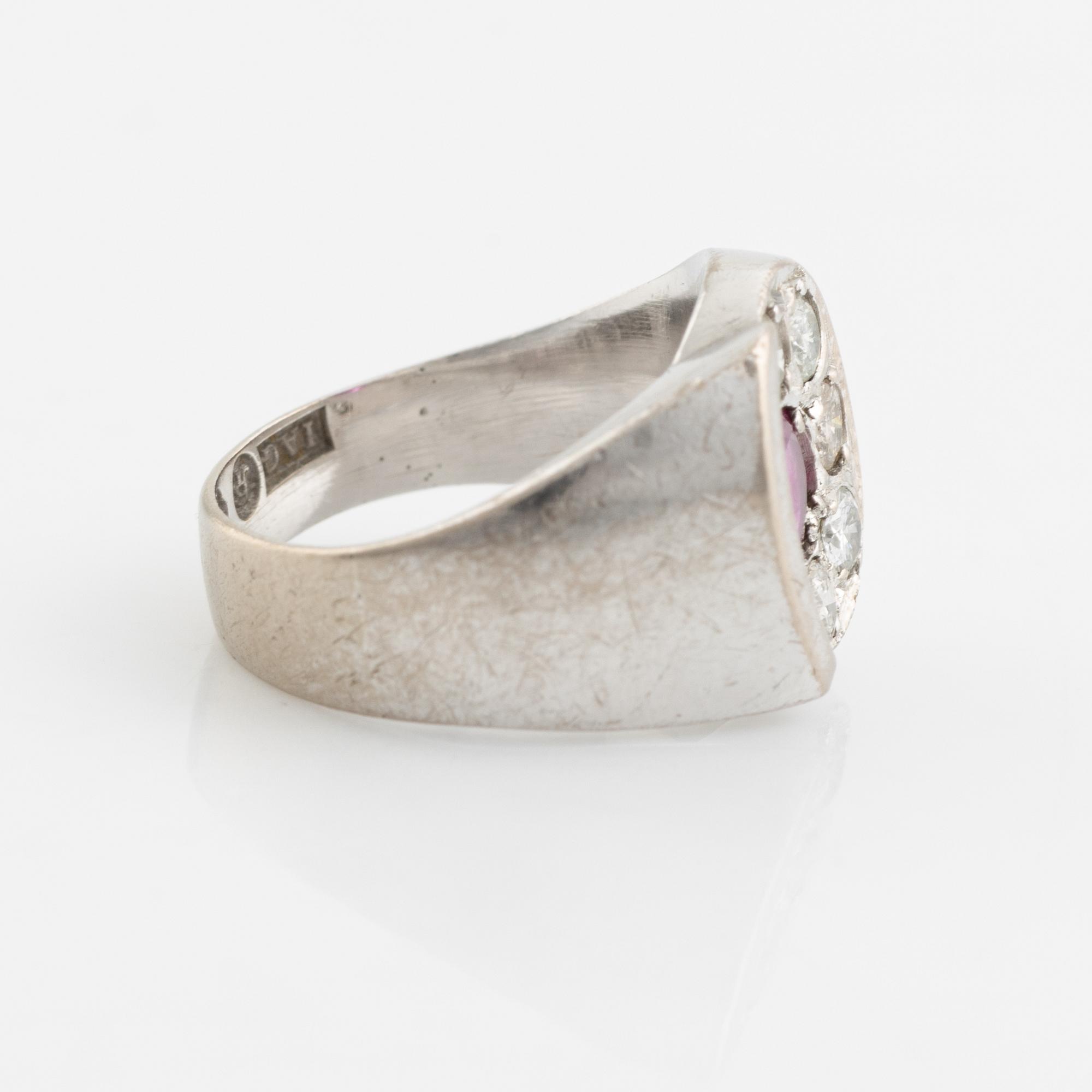 An 18K white gold ring set with a faceted ruby and round brilliant-cut diamonds.
