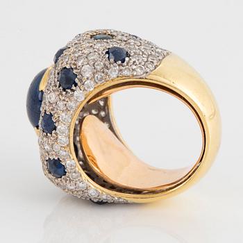 An 18K gold ring set with a cabochon-cut sapphire and round brilliant-cut diamonds and faceted sapphires.