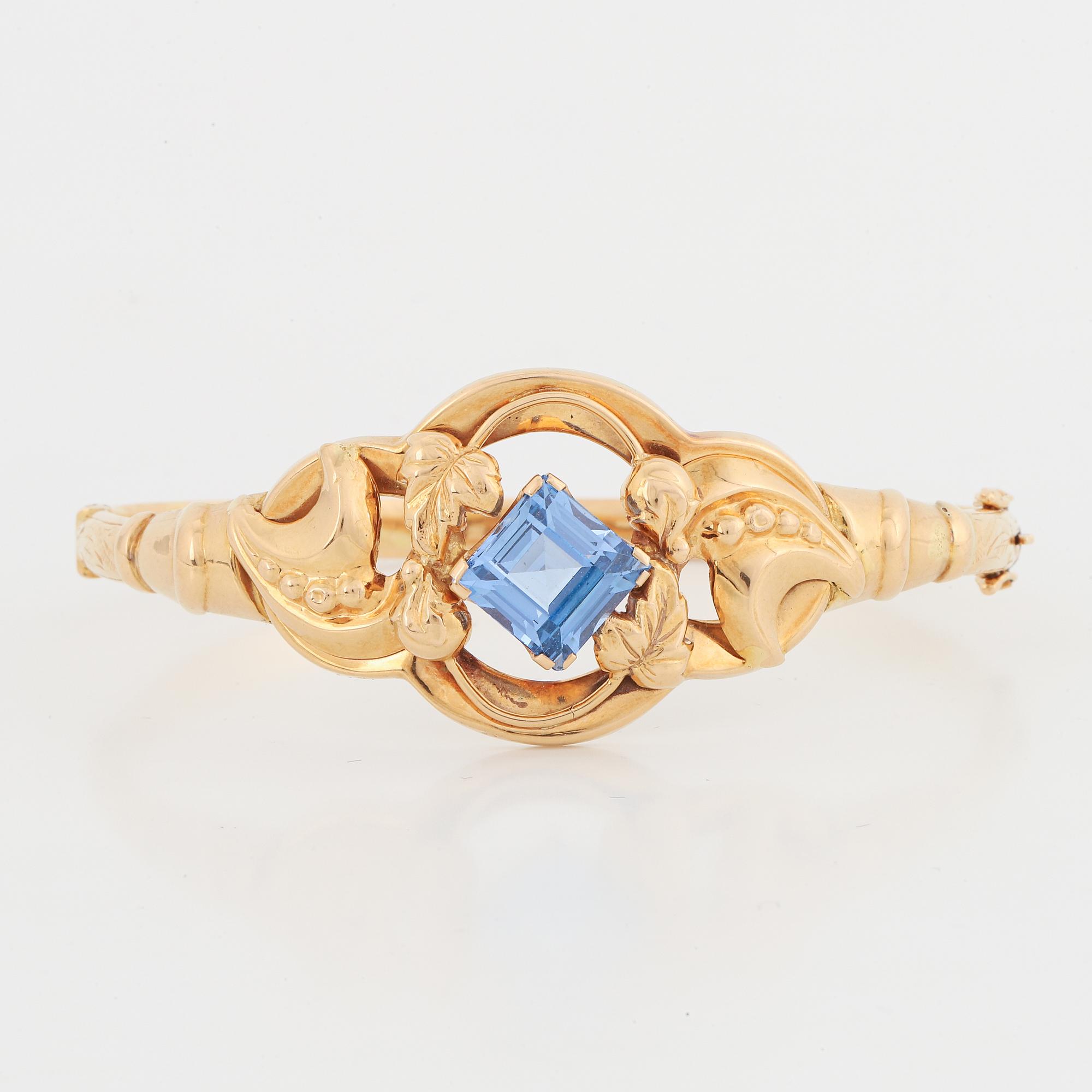 An 18K gold bangle set with a blue synthetic stone.