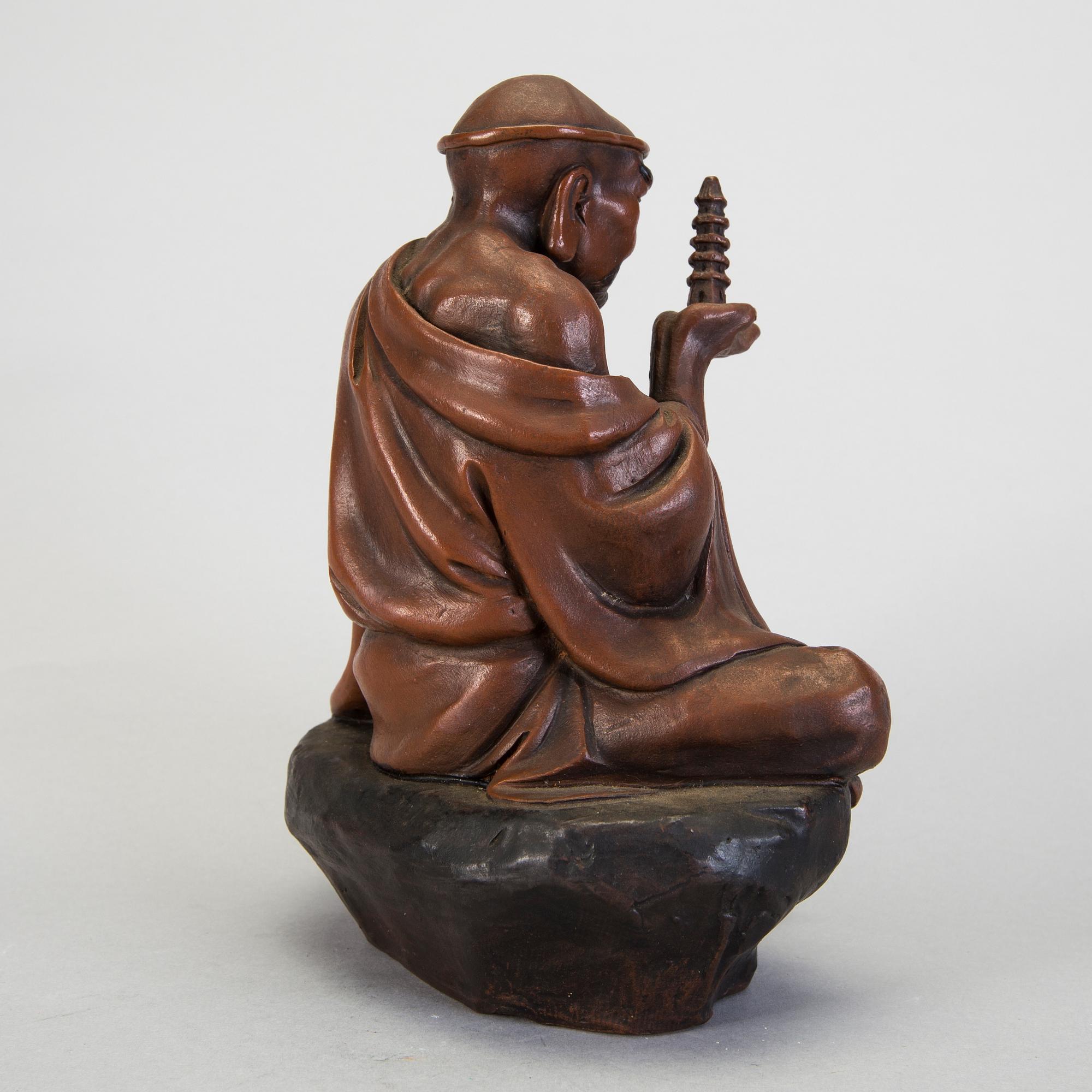 A Japanese earthenware seated figure of a man holding a pagoda, 20th century.