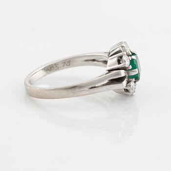 An 18K white gold ring set with a faceted emerald and round briliiant-cut diamonds.