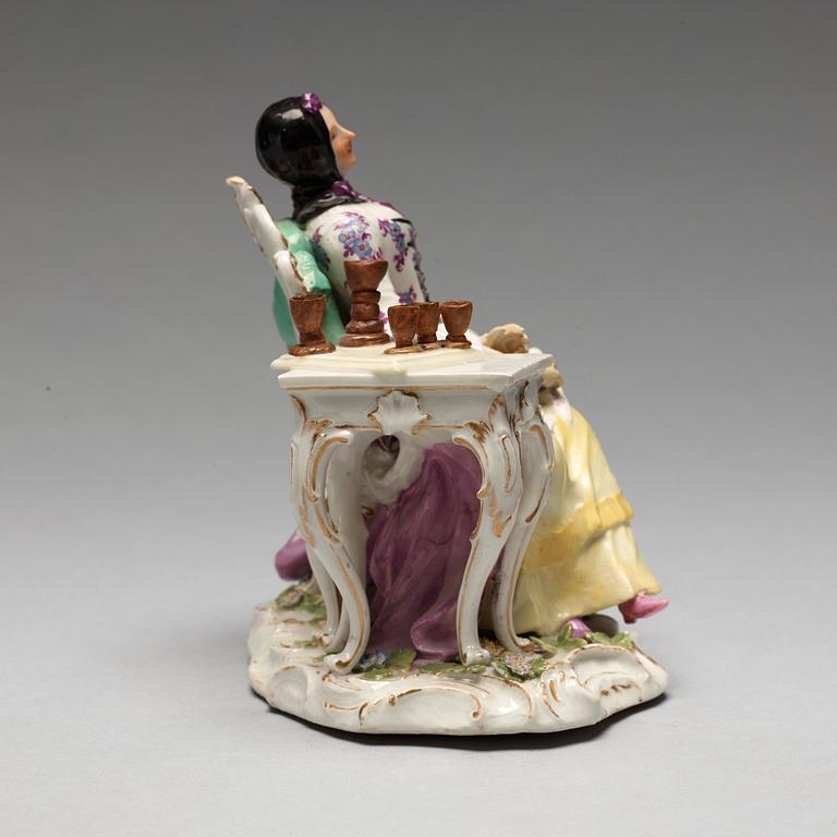 A Meissen porcelain figure of a lady by a table.