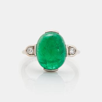 A platinum ring set with a cabochon-cut emerald and round brilliant-cut diamonds.