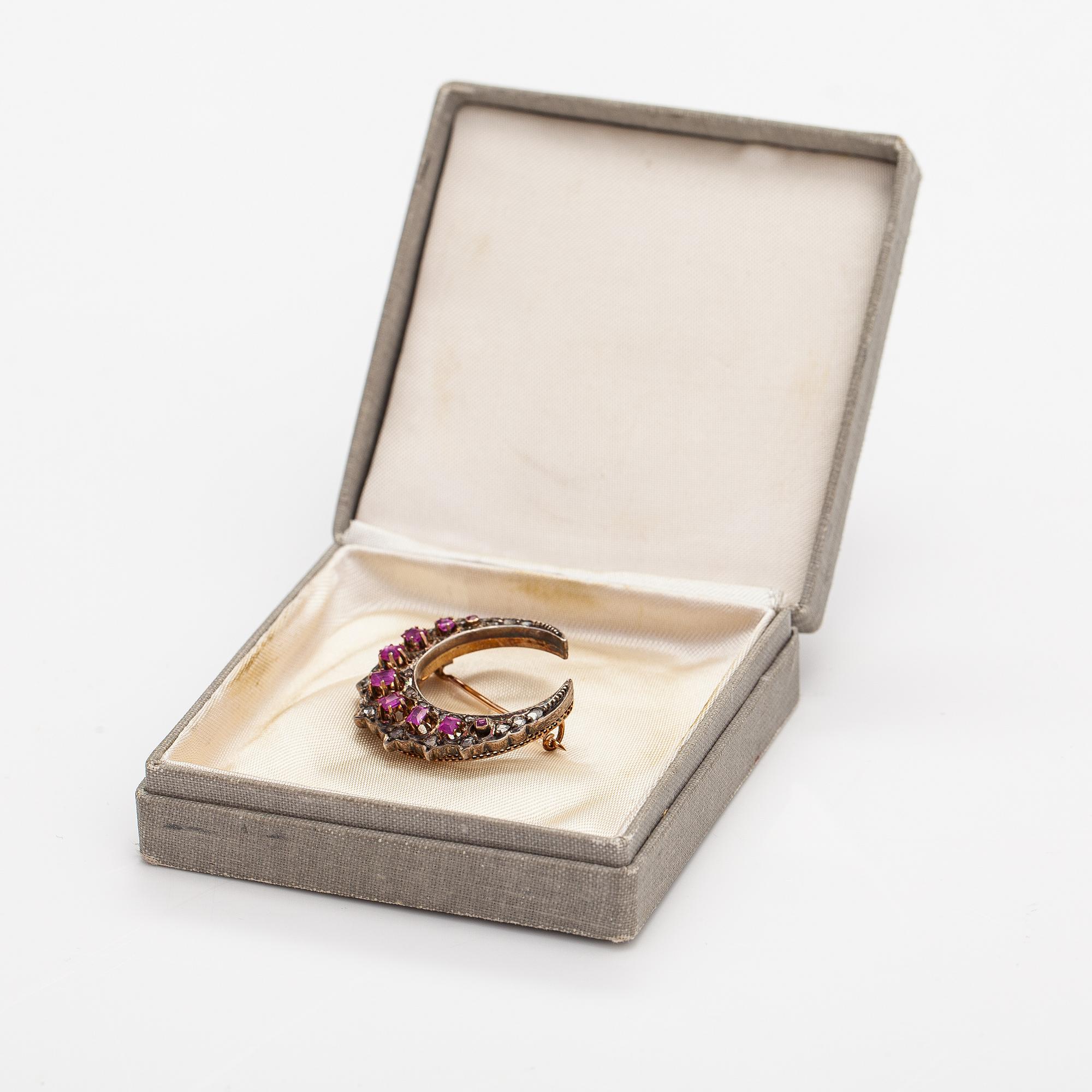 A cresent moon brooch made of 14K gold, silver, rubies and diamonds.