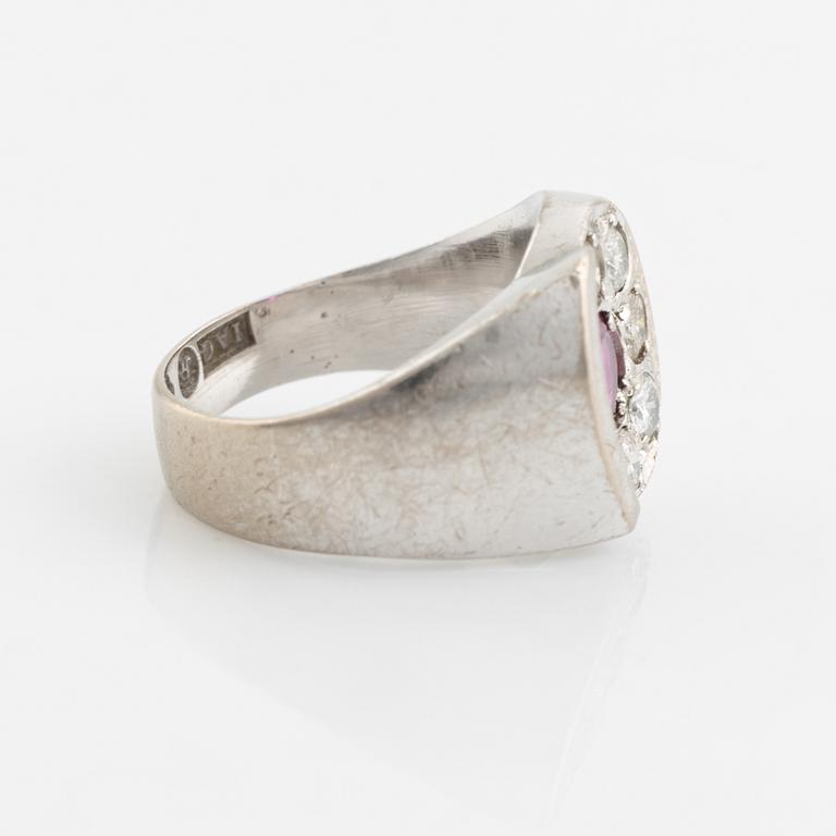 An 18K white gold ring set with a faceted ruby and round brilliant-cut diamonds.