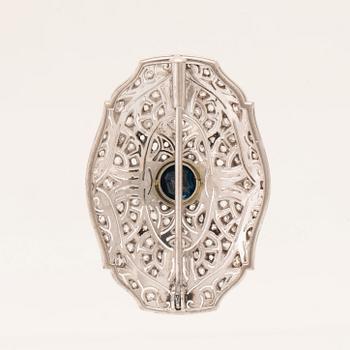 An 18K white gold brooch set with a facet-cut sapphire possibly synthetic, as well as brilliant and rose-cut diamonds.