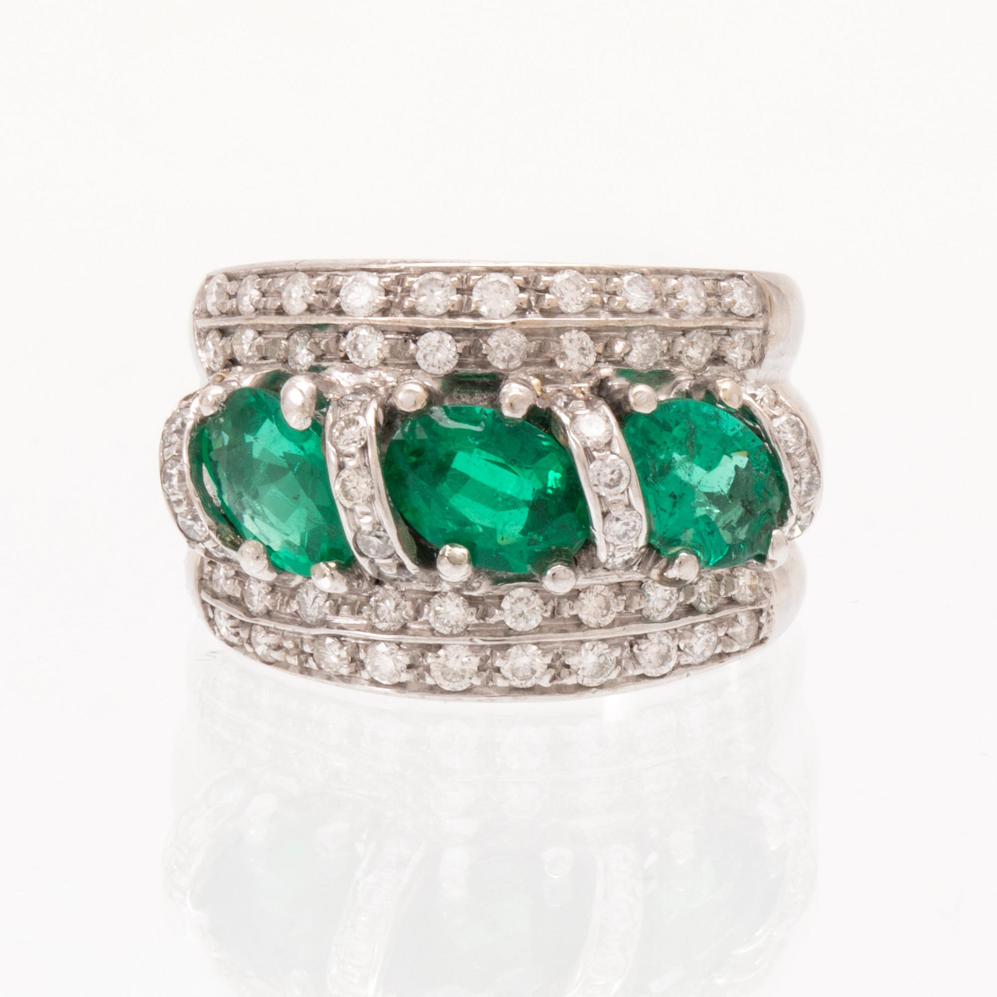 An 18K white gold ring set with oval cut emeralds and round brilliant cut diamonds.