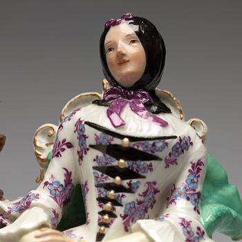 A Meissen porcelain figure of a lady by a table.