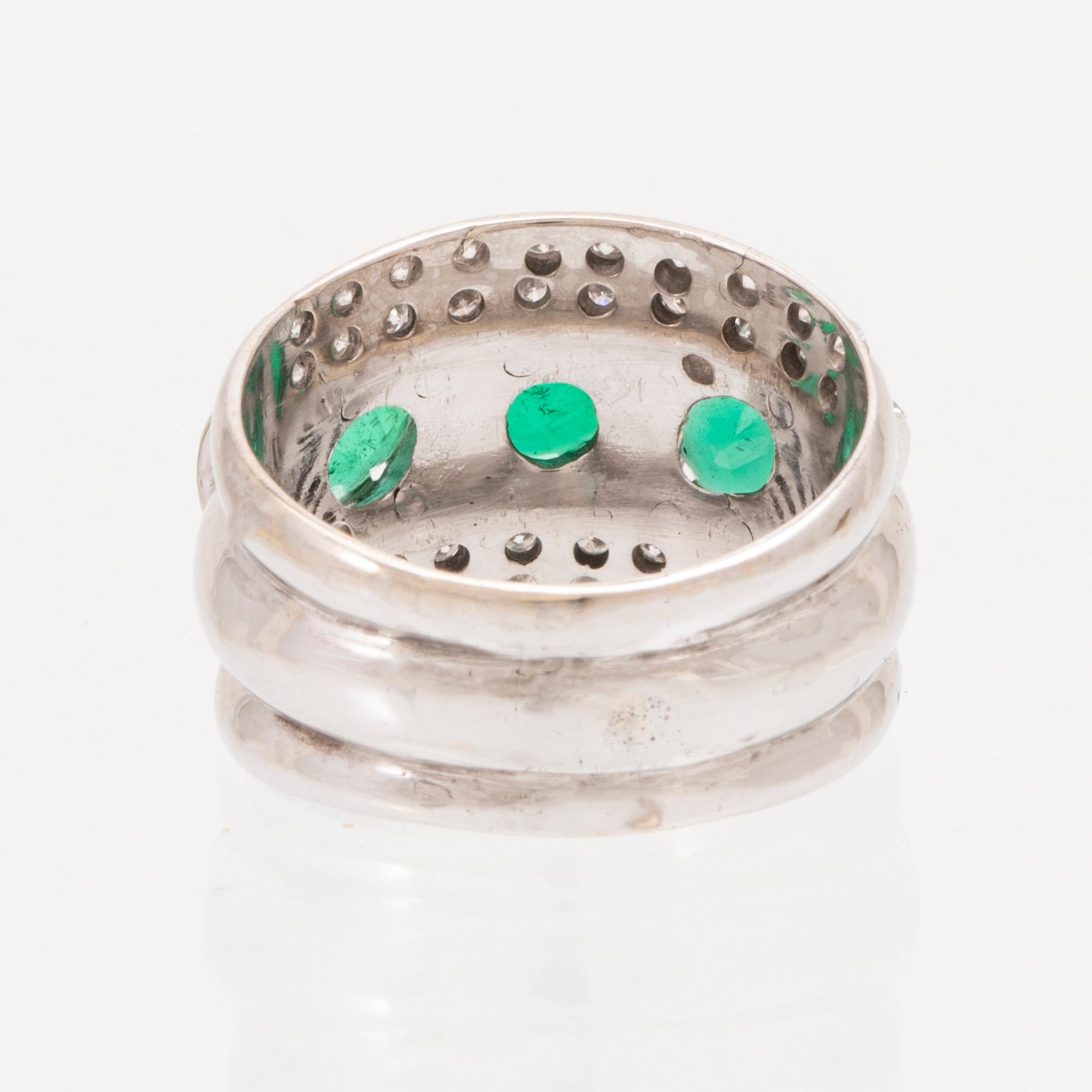 An 18K white gold ring set with oval cut emeralds and round brilliant cut diamonds.