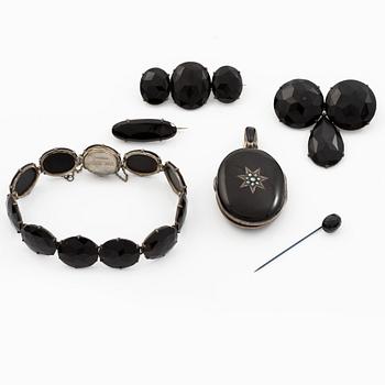 Collection of silver jewellery with black faceted stones, three brooches, a hat pin, a locket, and a bracelet.