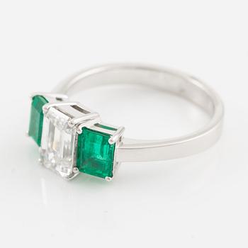 An 18K white gold ring set with an emerald-cut diamond and two step-cut emeralds.