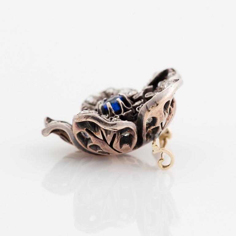 A silver and 14K gold brooch set with a blue stone and rose-cut diamonds.