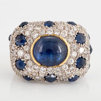 An 18K gold ring set with a cabochon-cut sapphire and round brilliant-cut diamonds and faceted sapphires.