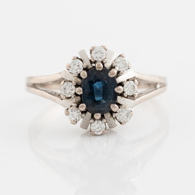 An 18K white gold ring set with a faceted sapphire and round brilliant-cut diamonds.