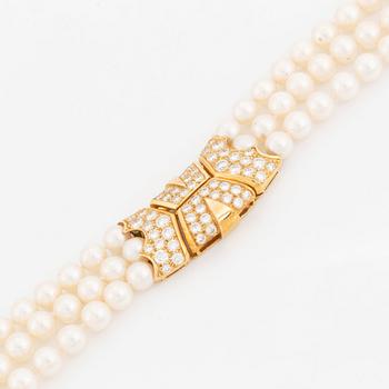 A Cartier triple strand cultured pearl necklace with an 18K gold clasp set with round brilliant-cut diamonds.