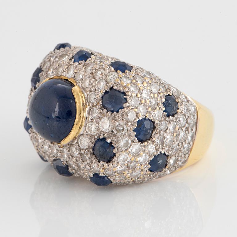 An 18K gold ring set with a cabochon-cut sapphire and round brilliant-cut diamonds and faceted sapphires.