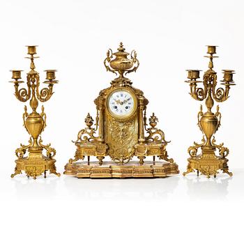 A mantle clock and a pair of candelabra, Louis XVI style, ca 1900.