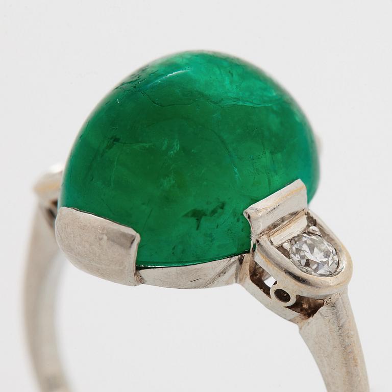 A platinum ring set with a cabochon-cut emerald and round brilliant-cut diamonds.