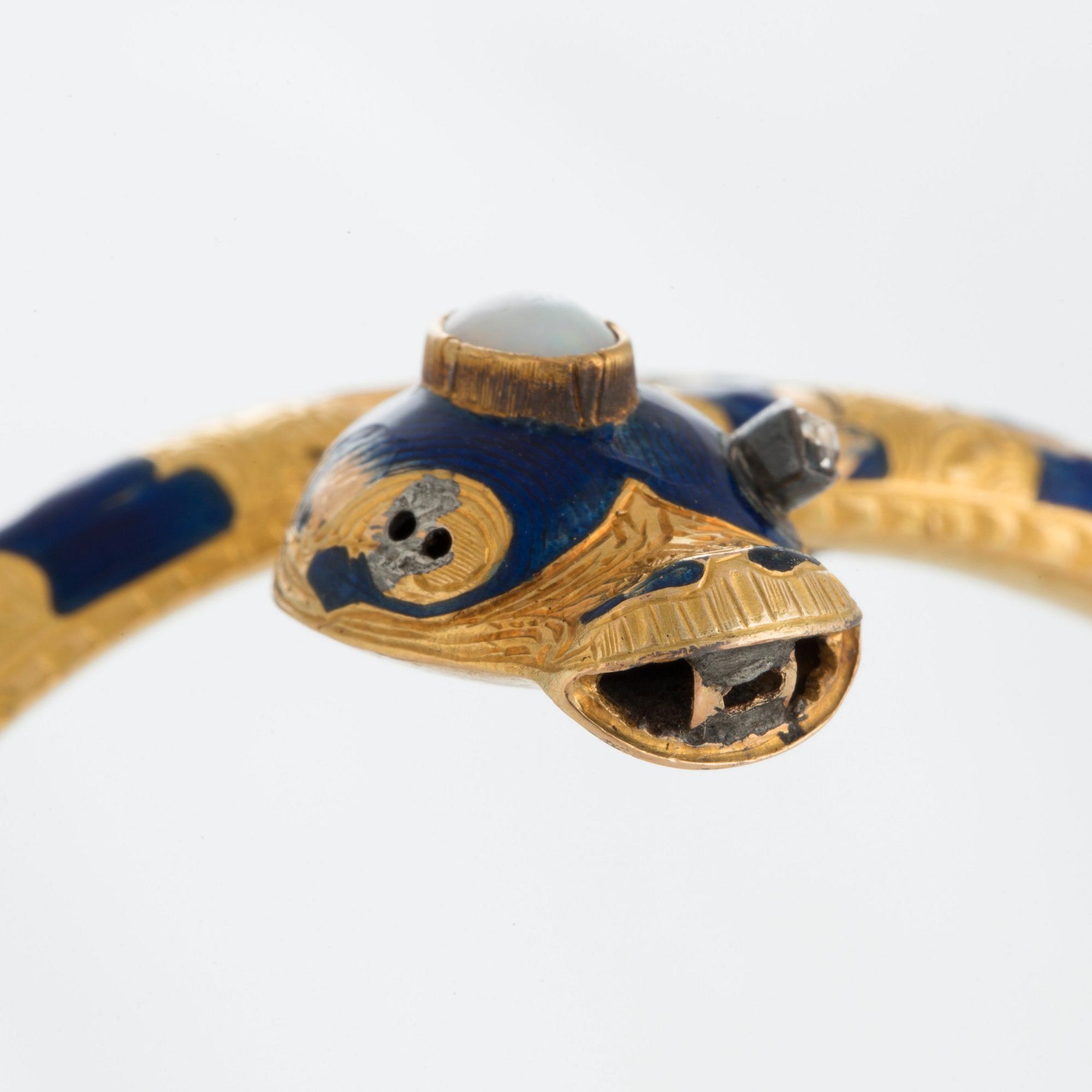 An 18K gold snake bangle decorated with blue enamel and set with an opal and a rose-cut diamond.