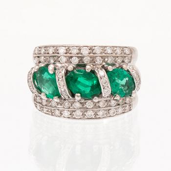 An 18K white gold ring set with oval cut emeralds and round brilliant cut diamonds.