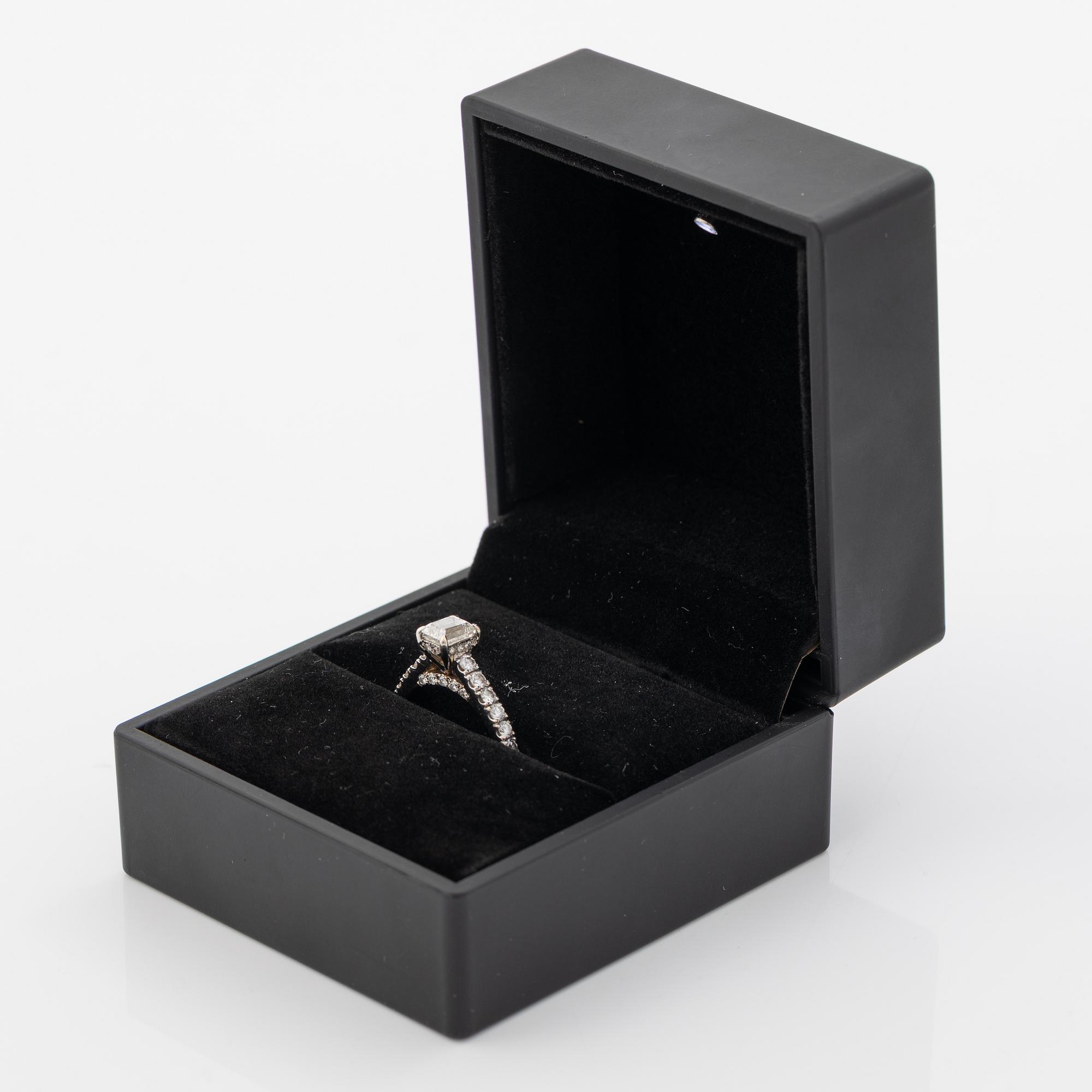 18K white gold ring set with an emerald-cut diamond and round brilliant-cut diamonds.