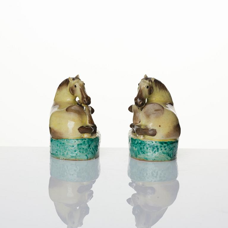A pair of green, yellow and aubergine glazed biscuit figures of recumbent horses, Qing dynasty.