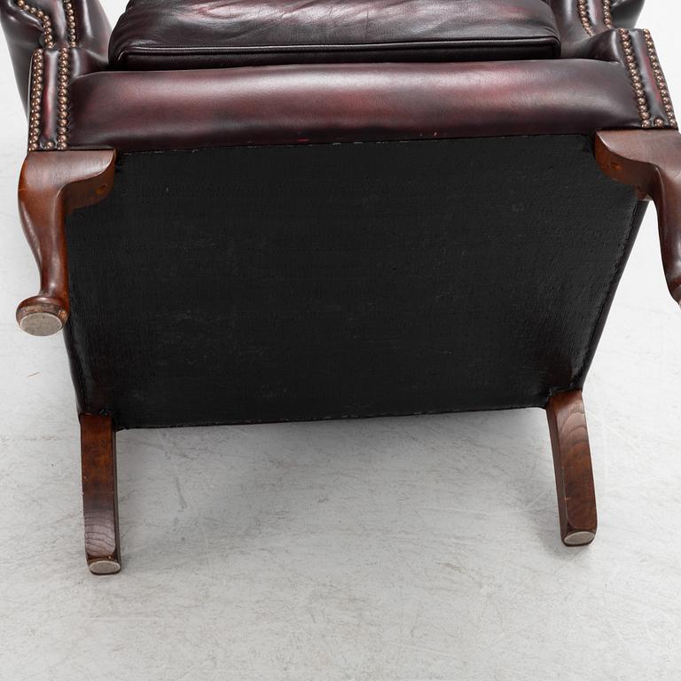 A leather upholstered wingback chair with stool. end of the 20th Century.