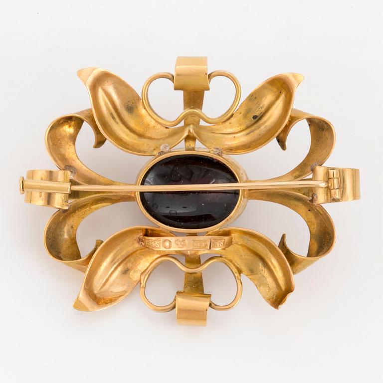 A brooch set with probably a cabochon-cut garnet.