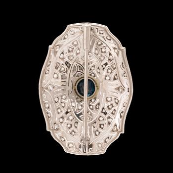 An 18K white gold brooch set with a facet-cut sapphire possibly synthetic, as well as brilliant and rose-cut diamonds.
