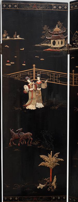 A chinese black lacquer six-panel screen, early 20th Century, with figures in gardens, inlays of carved mother of pearl, coloured bone, tree, and different stones. Back of panels with flowers painted in gold.