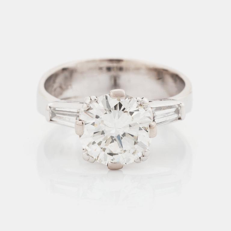 An 18K white gold ring set with a round brilliant-cut diamond and two tapered baguette-cut diamonds.