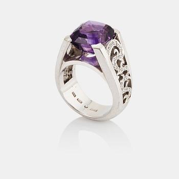 972. An 18K white gold ring set with a faceted amethyst and round brilliant-cut diamonds.