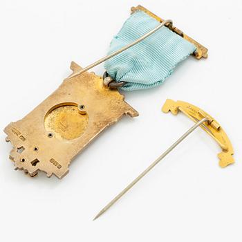 A jeton and pin, in gilded silver and 9 ct gold respectively.