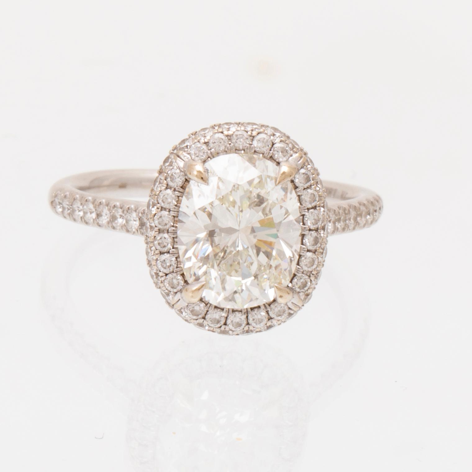 An 18K white gold ring by James Allen, set with an oval brilliant cut diamond in a halo of round brilliant cut diamonds.