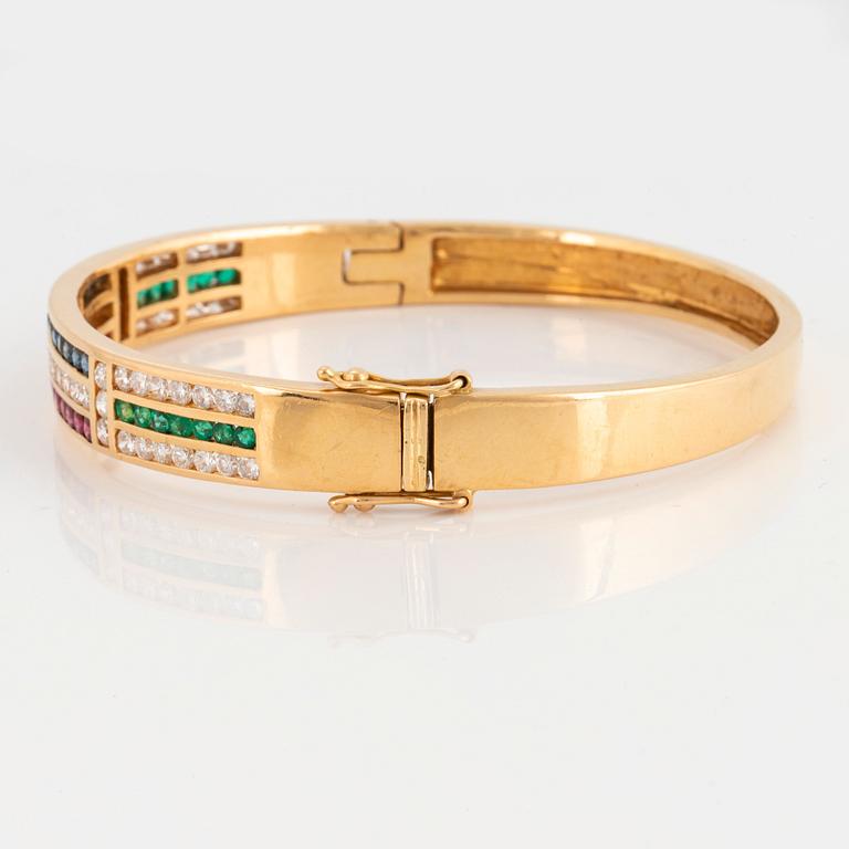 An 18K gold bangle set with round brilliant-cut diamonds, sapphires, emeralds and rubies.