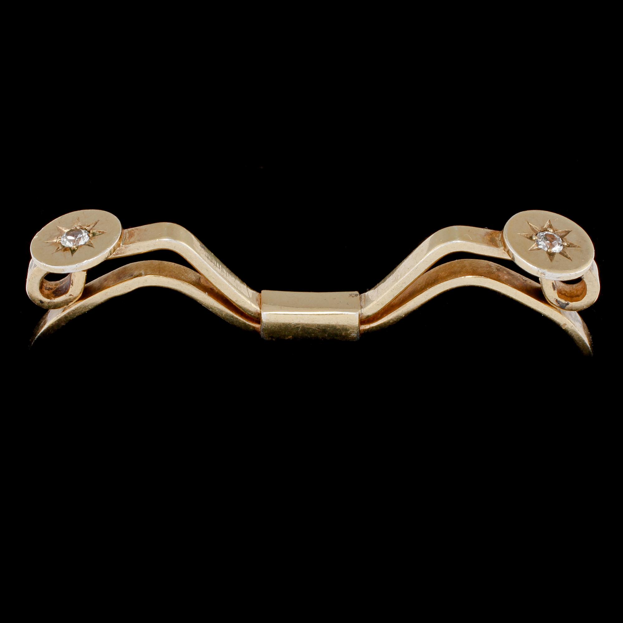 SPÄNNE, 18k guld med 2 briljantslipade vita stenar, Nils Ahlström, Borås, 1953. Vikt 6 g.