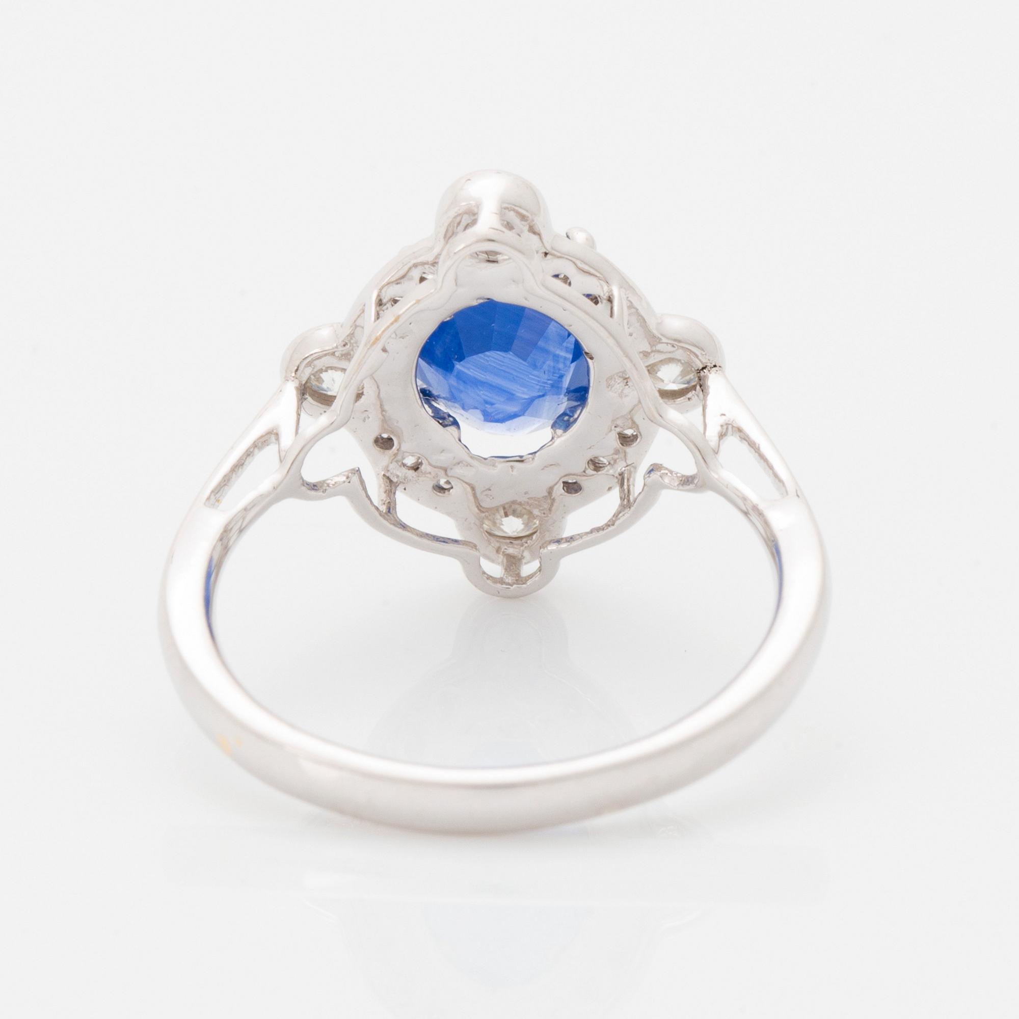 An 18K white gold ring set with a faceted sapphire and round brilliant-cut diamonds.