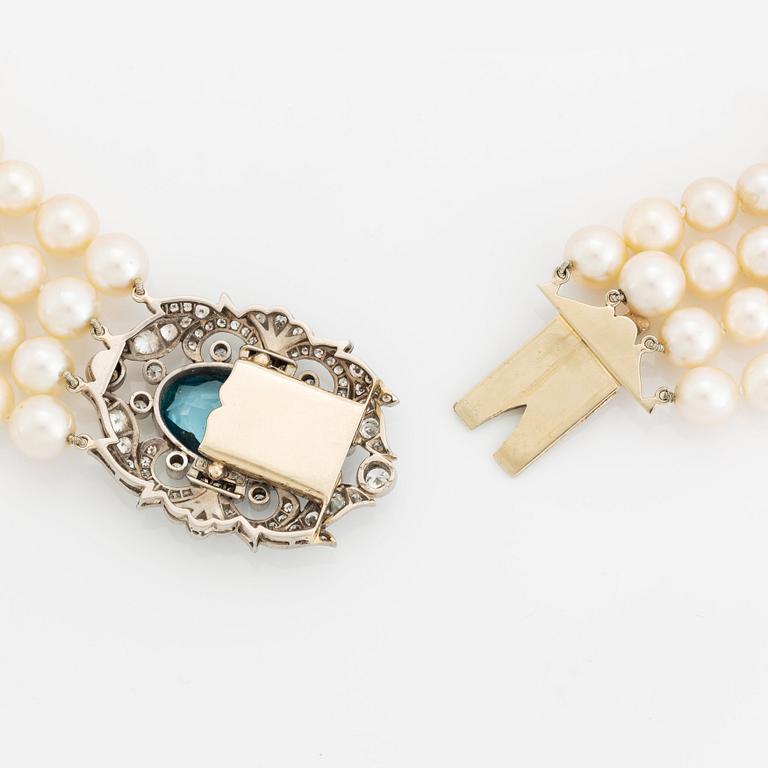 A four strand cultured pearl necklace with a clasp in 14K gold set with a faceted aquamarine.