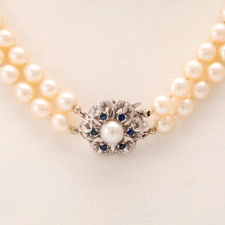 A double-stranded necklace of cultured pearls and an 18K white gold clasp with blue stones.