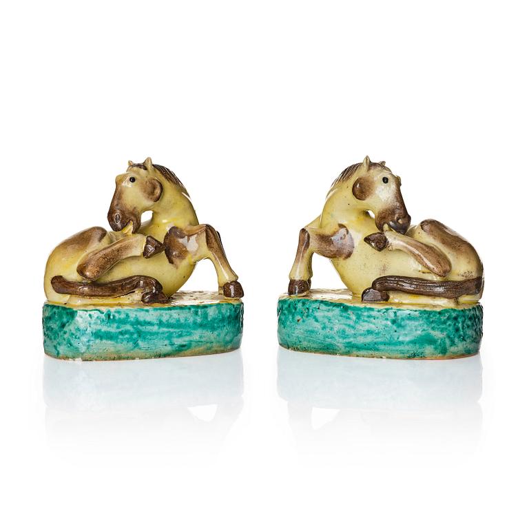 A pair of green, yellow and aubergine glazed biscuit figures of recumbent horses, Qing dynasty.