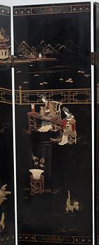 A chinese black lacquer six-panel screen, early 20th Century, with figures in gardens, inlays of carved mother of pearl, coloured bone, tree, and different stones. Back of panels with flowers painted in gold.