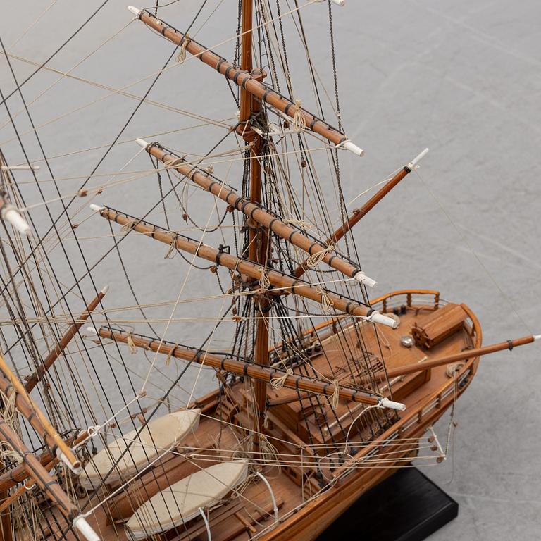A wooden scale model of Cutty Sark on a painted wooden stand.
