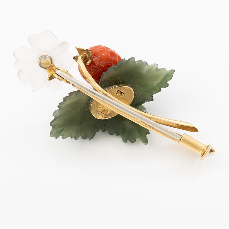 A flower brooch 18K gold with coral, rock crystal, a green stone likely nephrite, and a round brilliant-cut diamond.