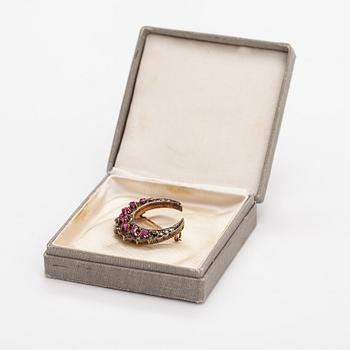 A cresent moon brooch made of 14K gold, silver, rubies and diamonds.