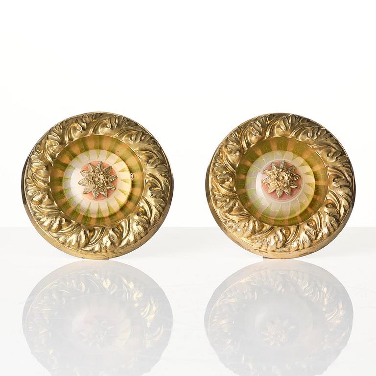 A pair of presumably English Empire repoussé gilt-brass and painted glass curtain tiebacks, early 19th century.
