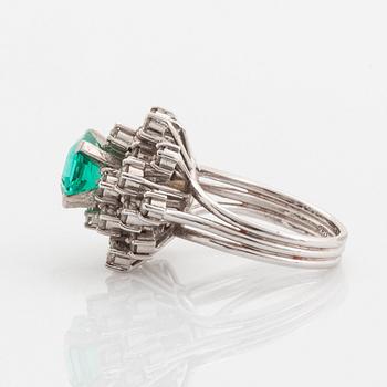 A platinum ring set with a faceted emerald and round brilliant-cut diamonds.