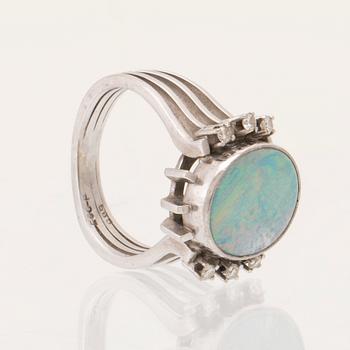 A 14K white gold ring set with an opal doublet or triplet and round brilliant-cut diamonds.