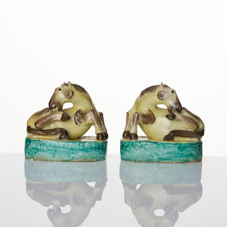 A pair of green, yellow and aubergine glazed biscuit figures of recumbent horses, Qing dynasty.