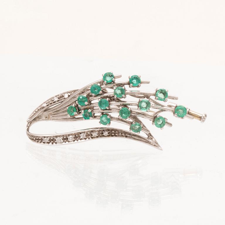 An 18K white gold brooch with round brilliant cut emeralds and single cut diamonds.